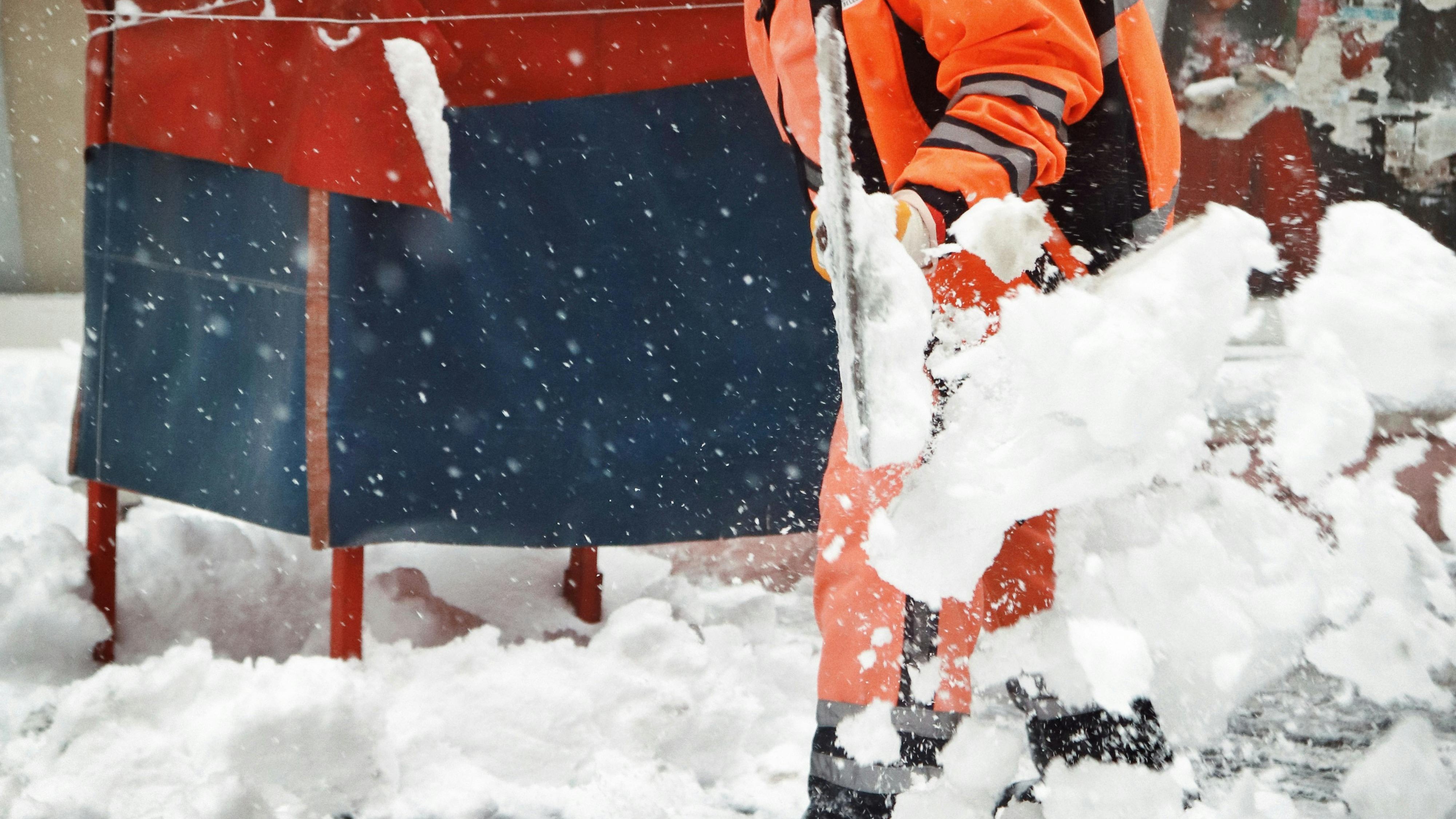Mitarbeiter schaufelt bei starkem Schneefall eine Einfahrt frei
