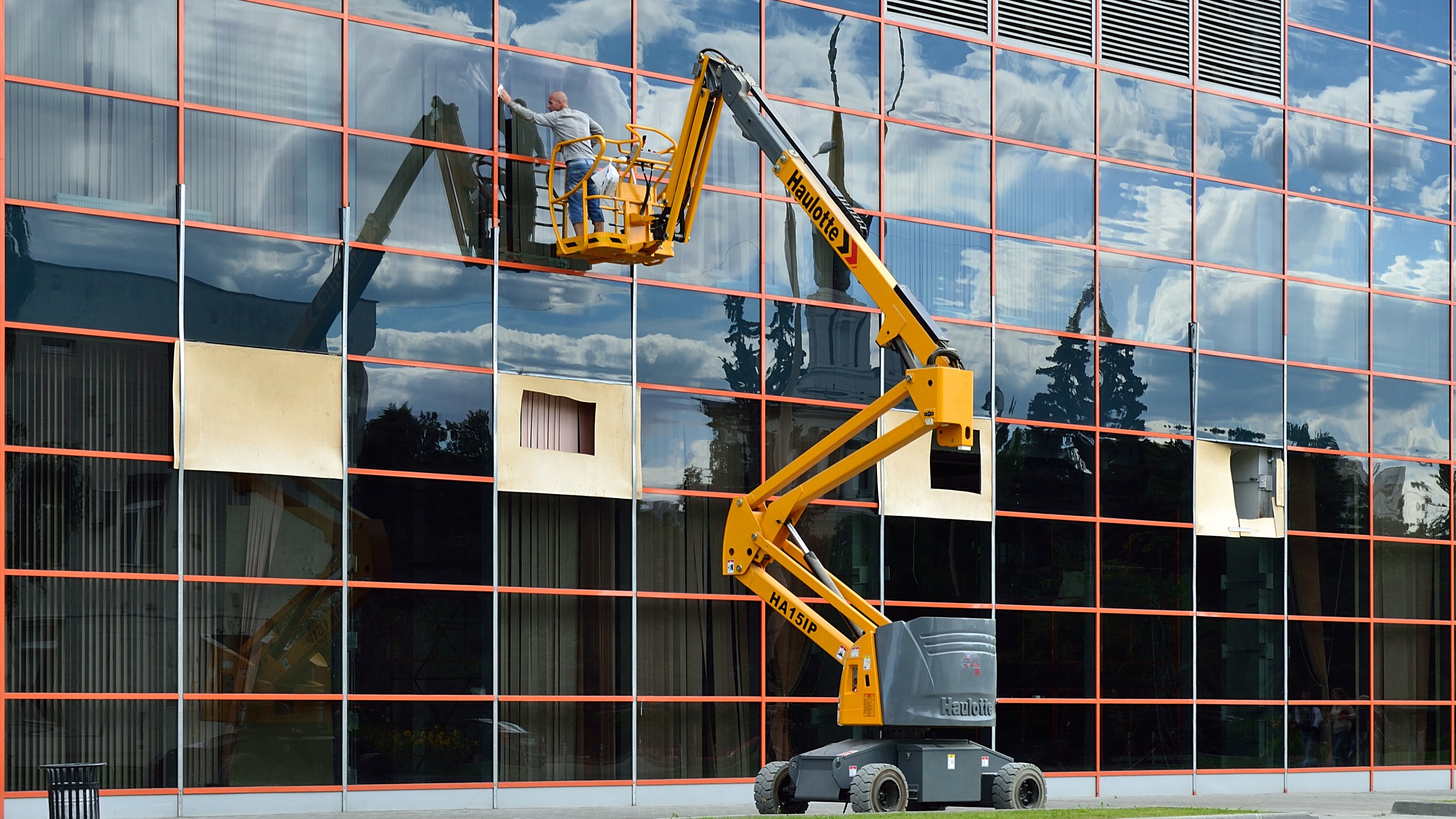 Fensterreinigung Mitarbeiter reinigt mit einer Hubarbeitsbühne die Fensterfront eines Gebäudes